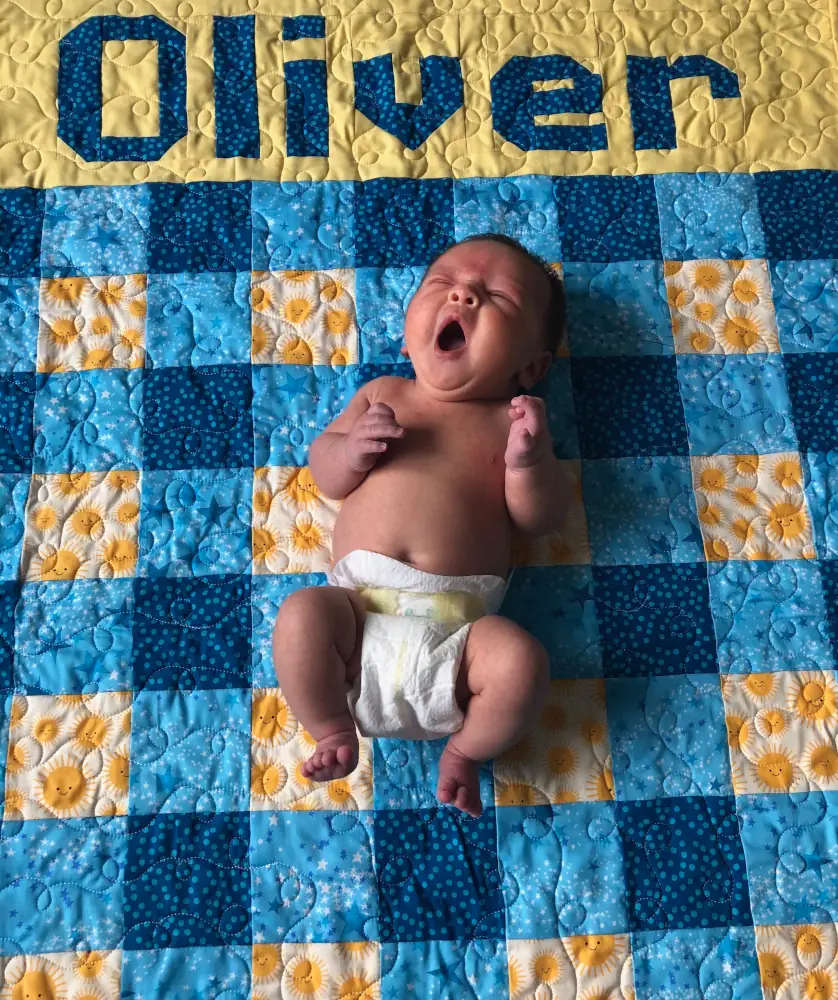 A baby laying on a quilt with the name oliver on it