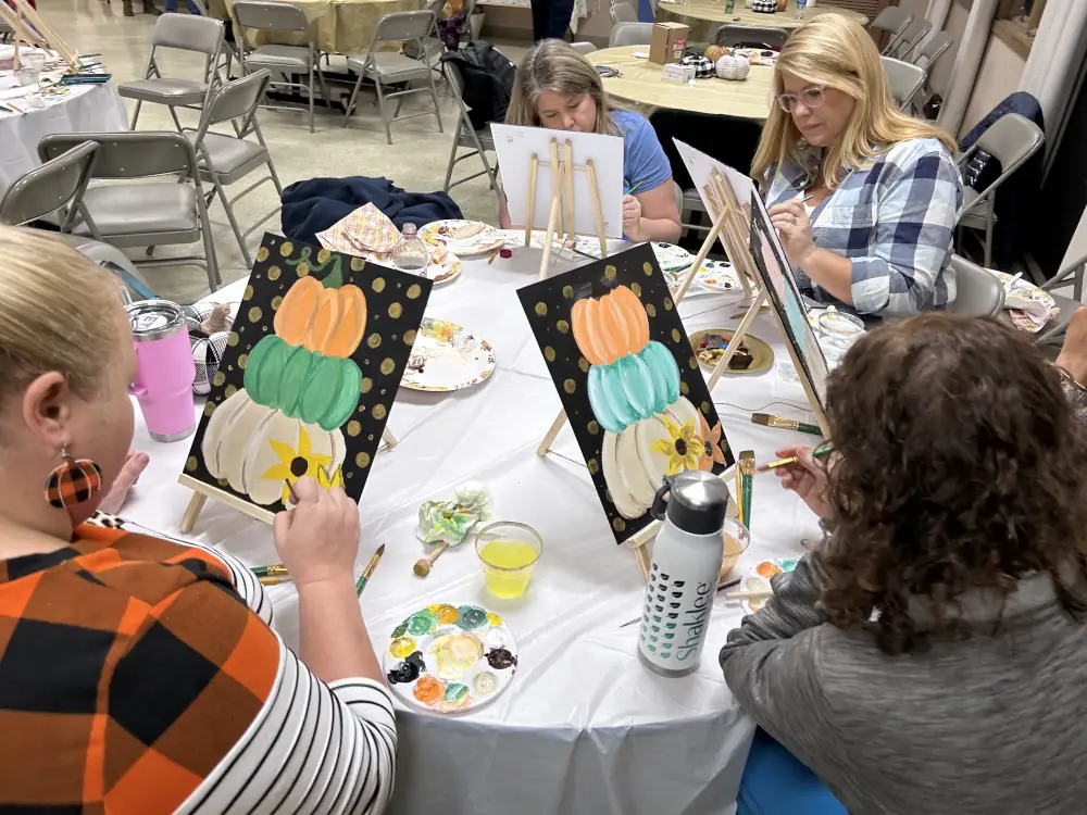 A group of adults at a round table painting on small easles