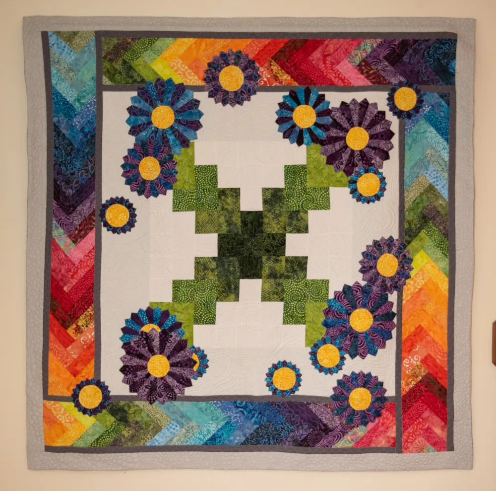 a colorful quilt with a rainbow border hanging on the wall